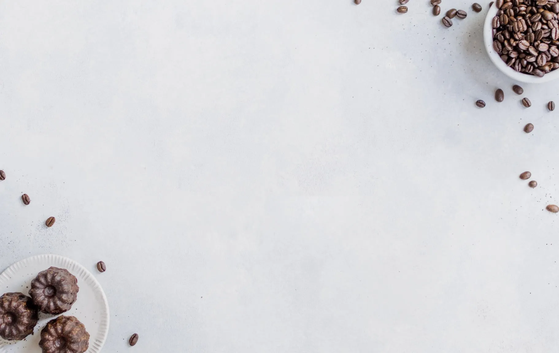 Coffee beans and small chocolate cakes arranged around the edge of a bright, empty surface