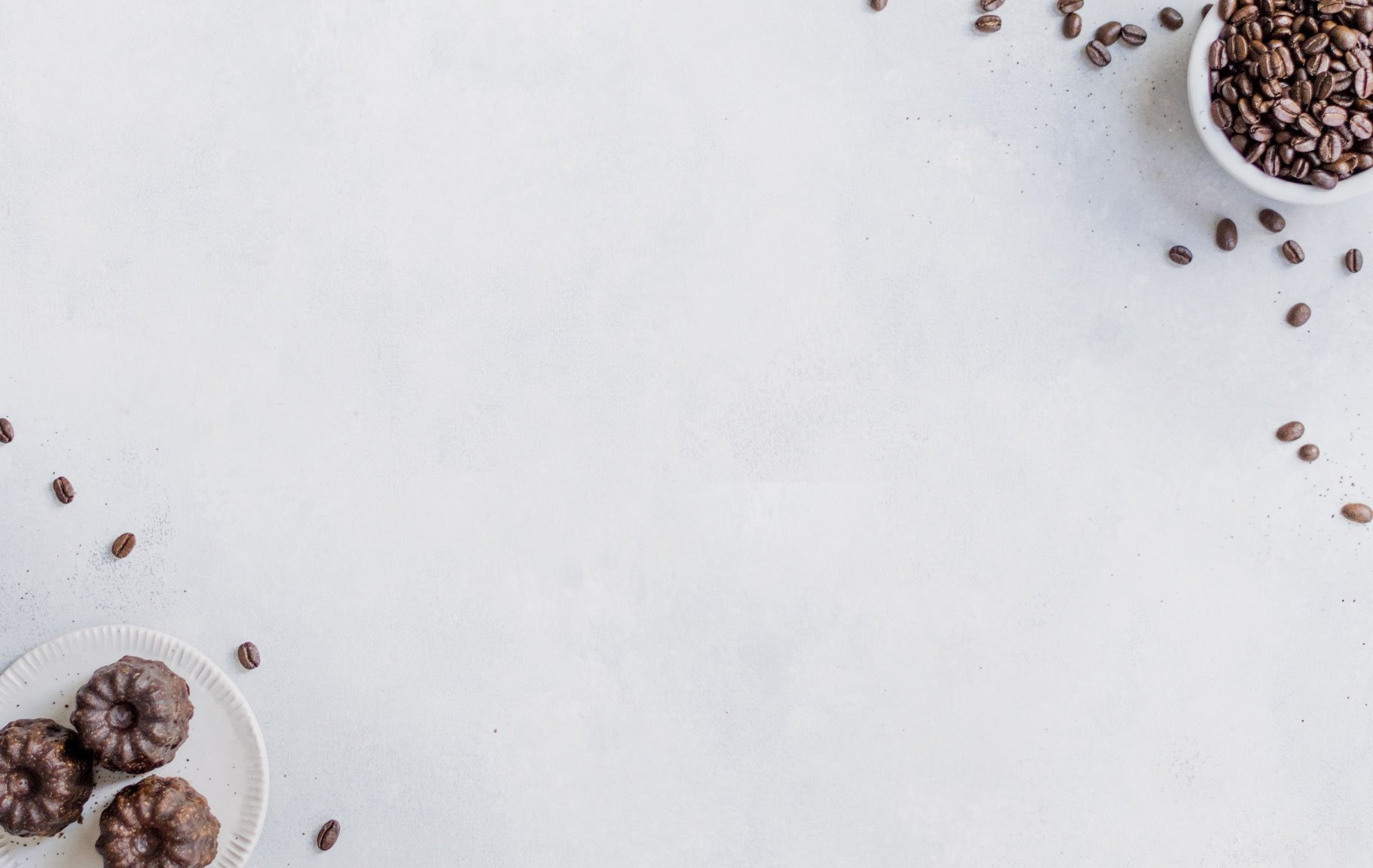 Coffee beans and small chocolate cakes arranged around the edge of a bright, empty surface